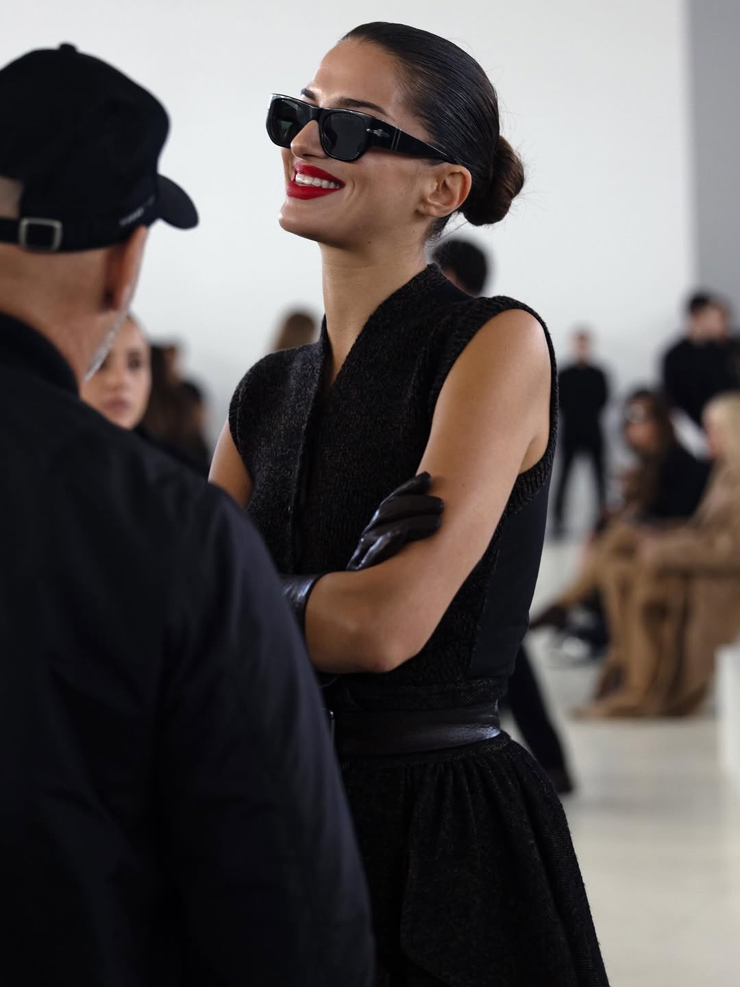 Woman in a black dress and sunglasses standing in a fashion show setting