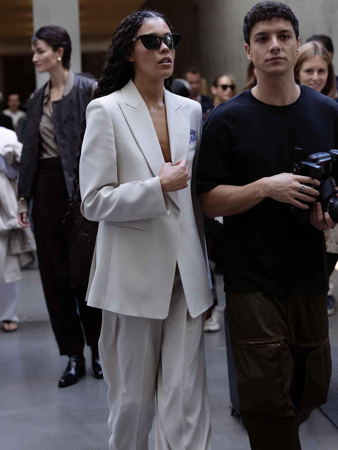Person wearing a white suit with a visible brand logo, standing in an urban setting.