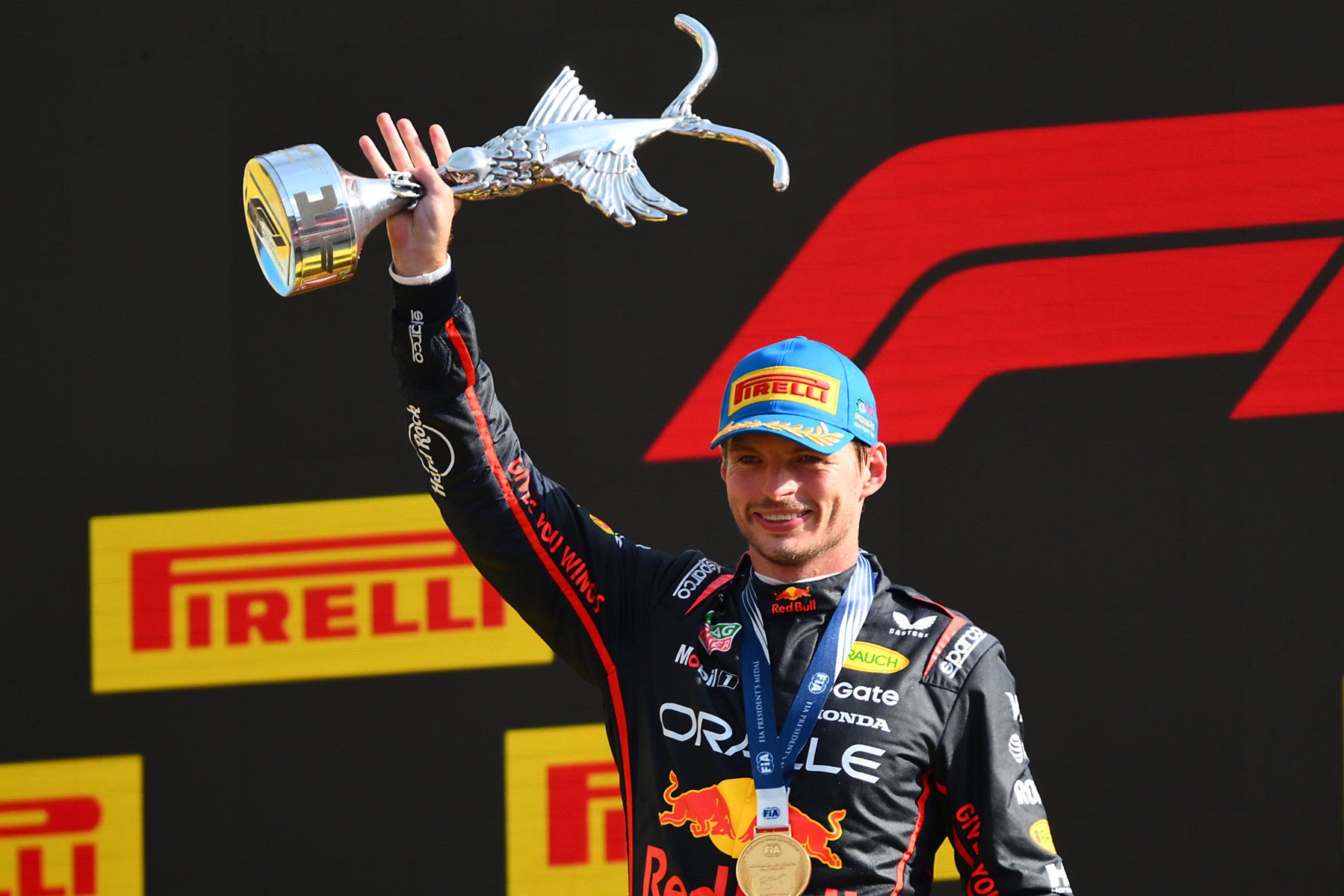 Max Verstappen in racing suit holding the Monza 2025 Formula 1 trophy with Pirelli and F1 logos in the background