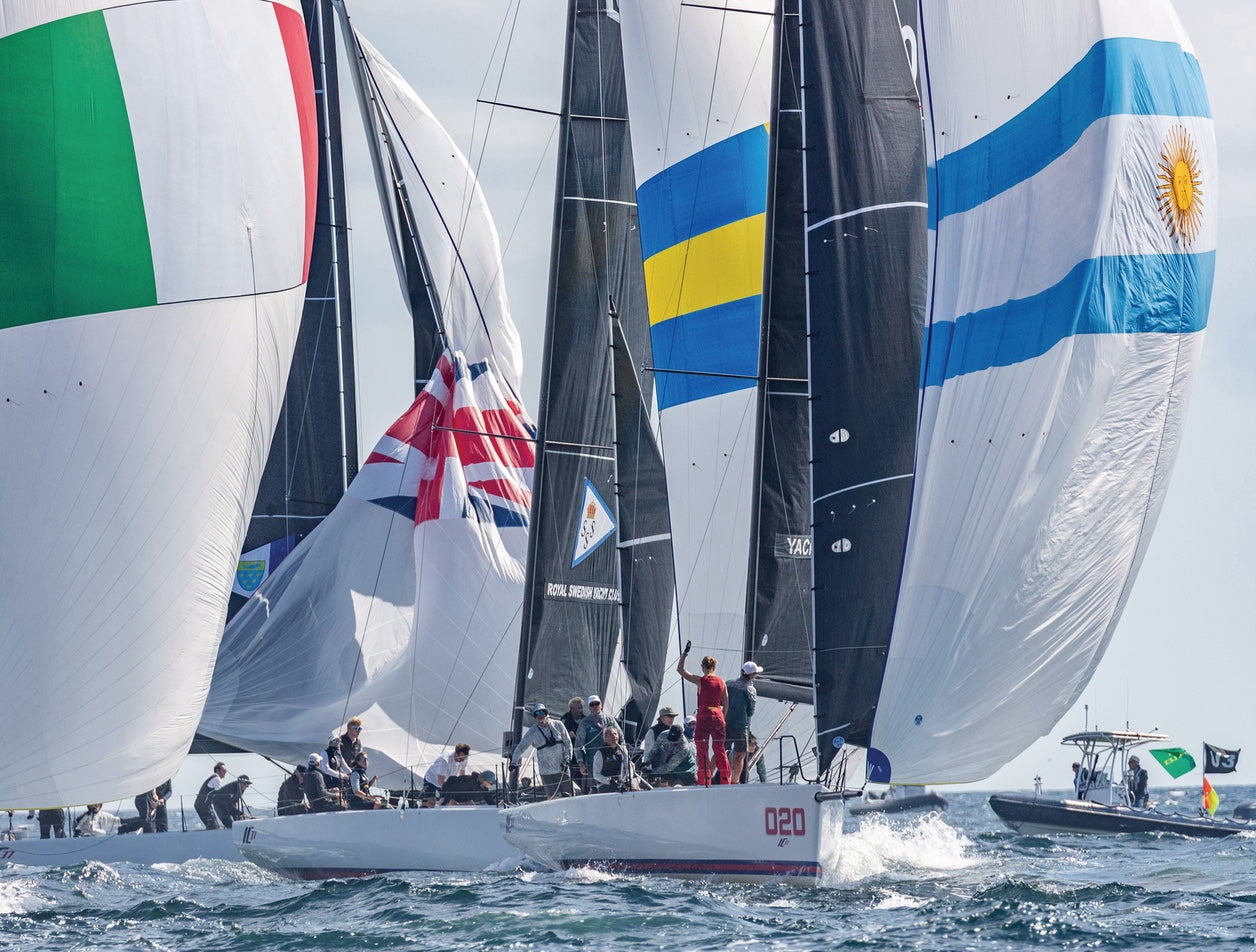 Sailing race with boats featuring various national flags on a sunny day.