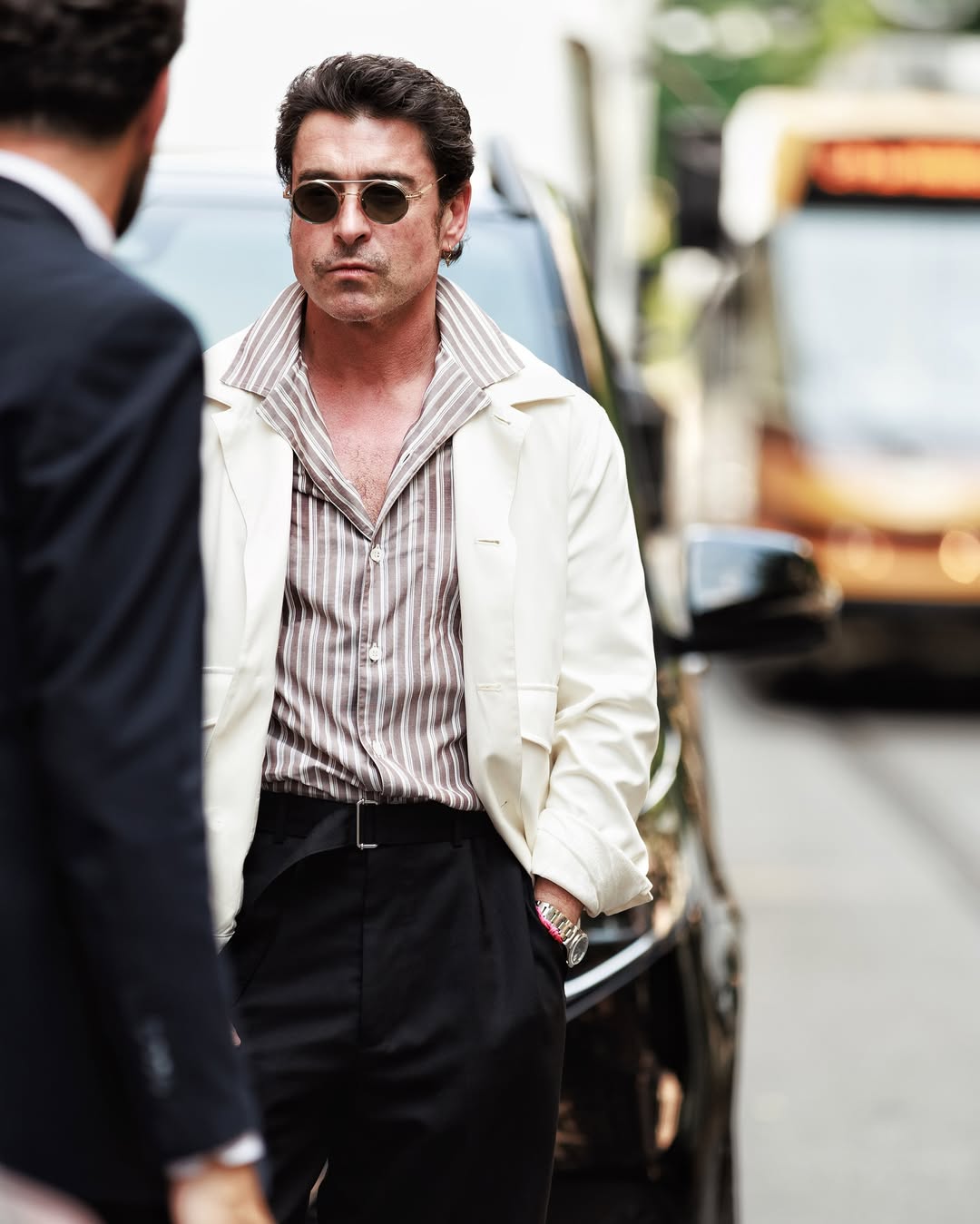 Man wearing sunglasses and a white jacket on a city street