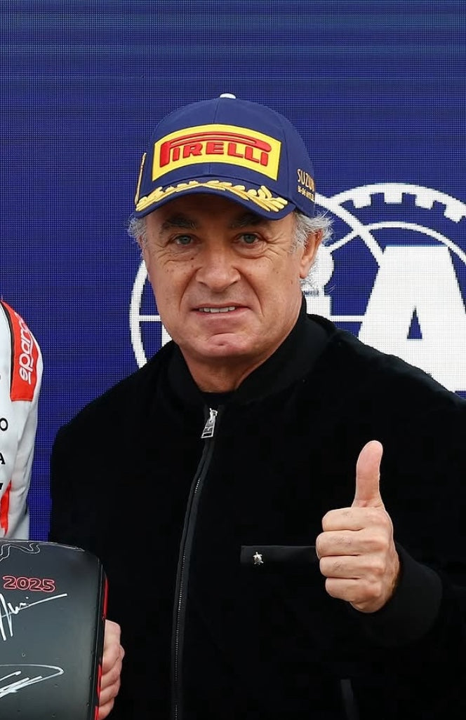 Jean Alesi wearing a Pirelli cap and giving a thumbs-up in front of a Pirelli logo.