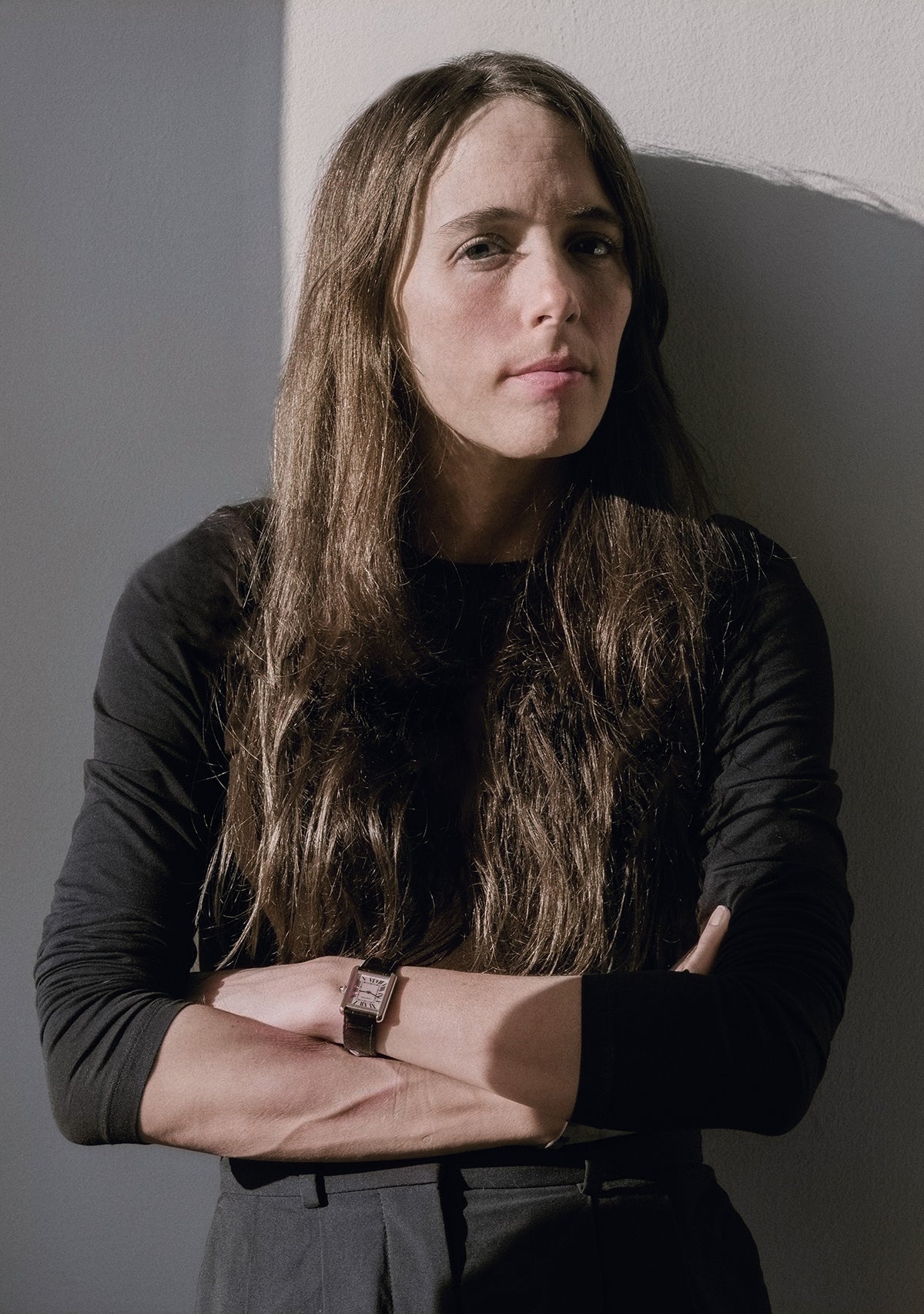 Person with long hair wearing a black shirt against a gray wall