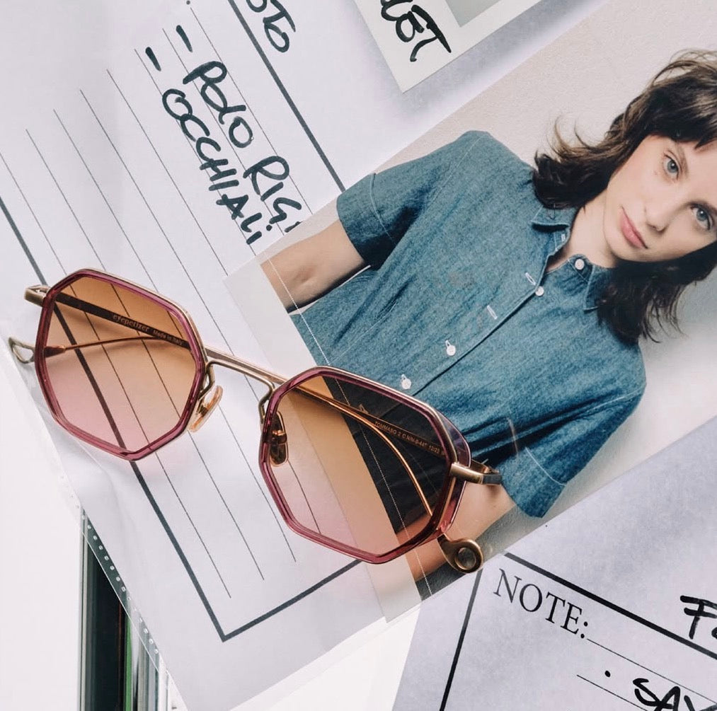 Sunglasses with a maroon gradient lens on a magazine with a person wearing a denim shirt.