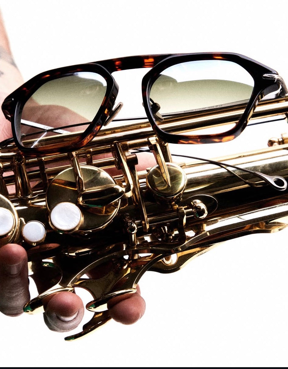 Gold saxophone with sunglasses on top against a white background