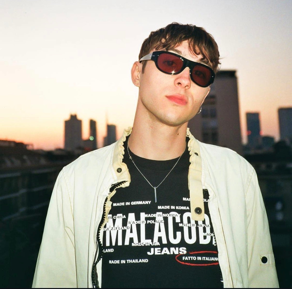 Person wearing sunglasses and a Malacoba jeans shirt with a cityscape background