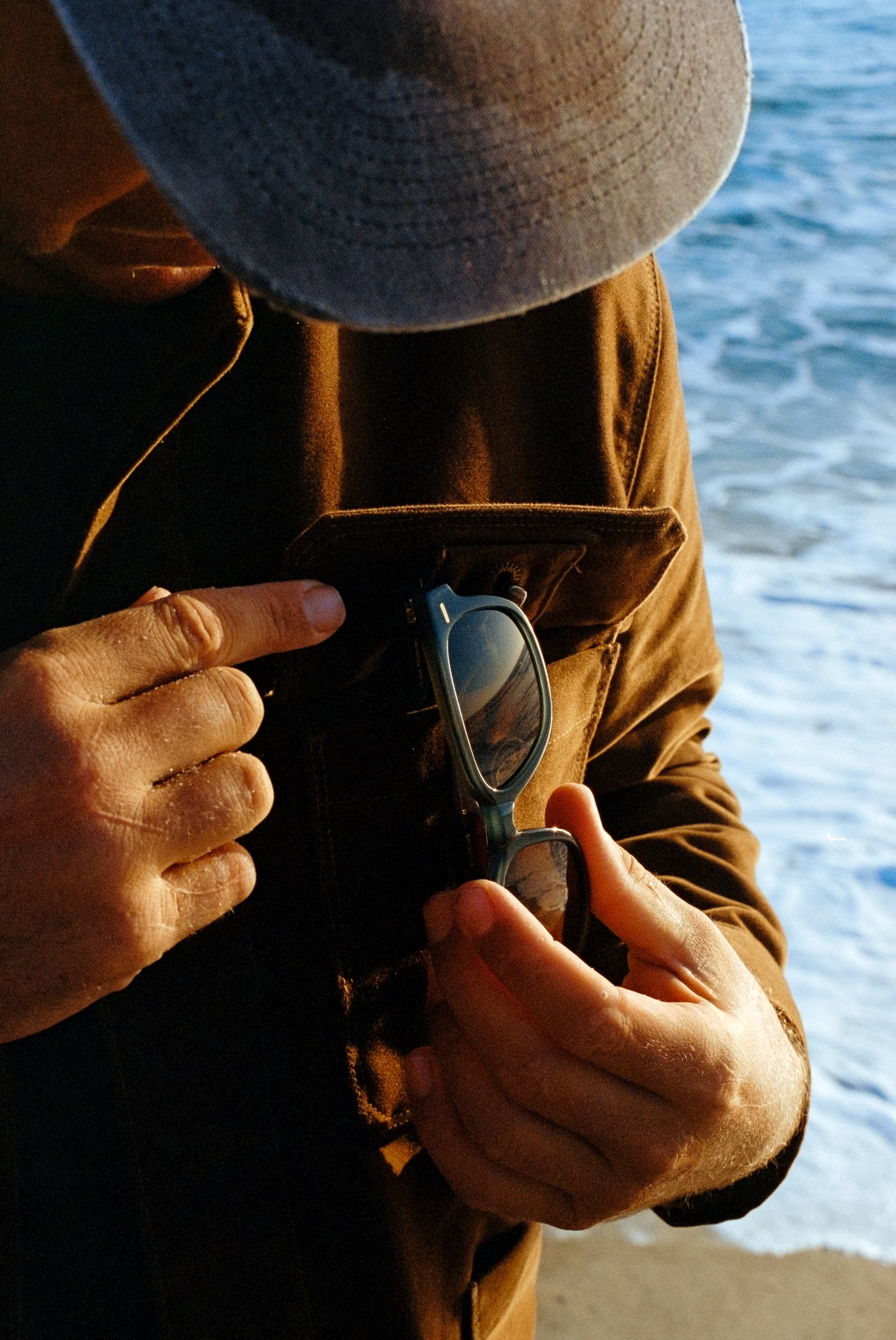 Person holding sunglasses with a blurred background of water