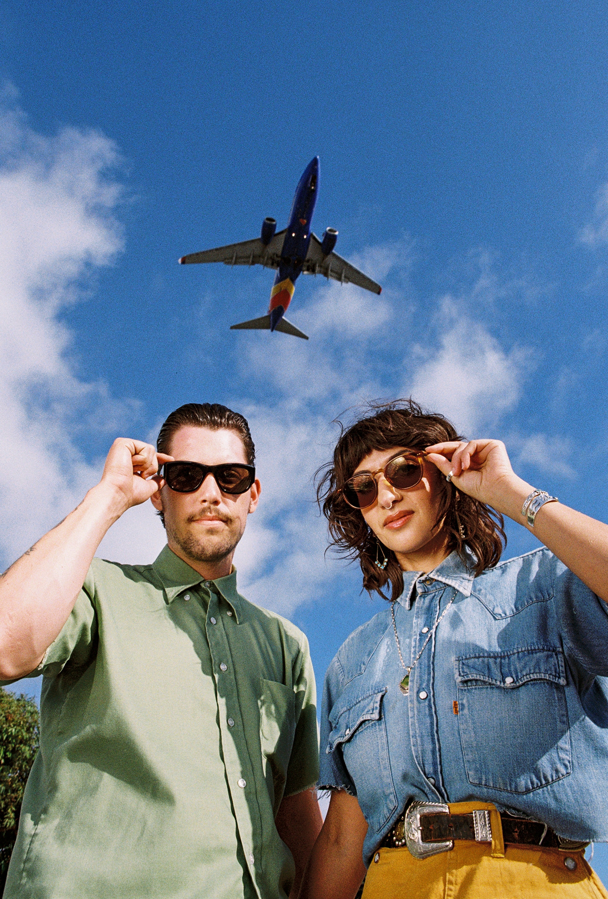 Two people wearing sunglasses with a Southwest airplane flying in the sky.