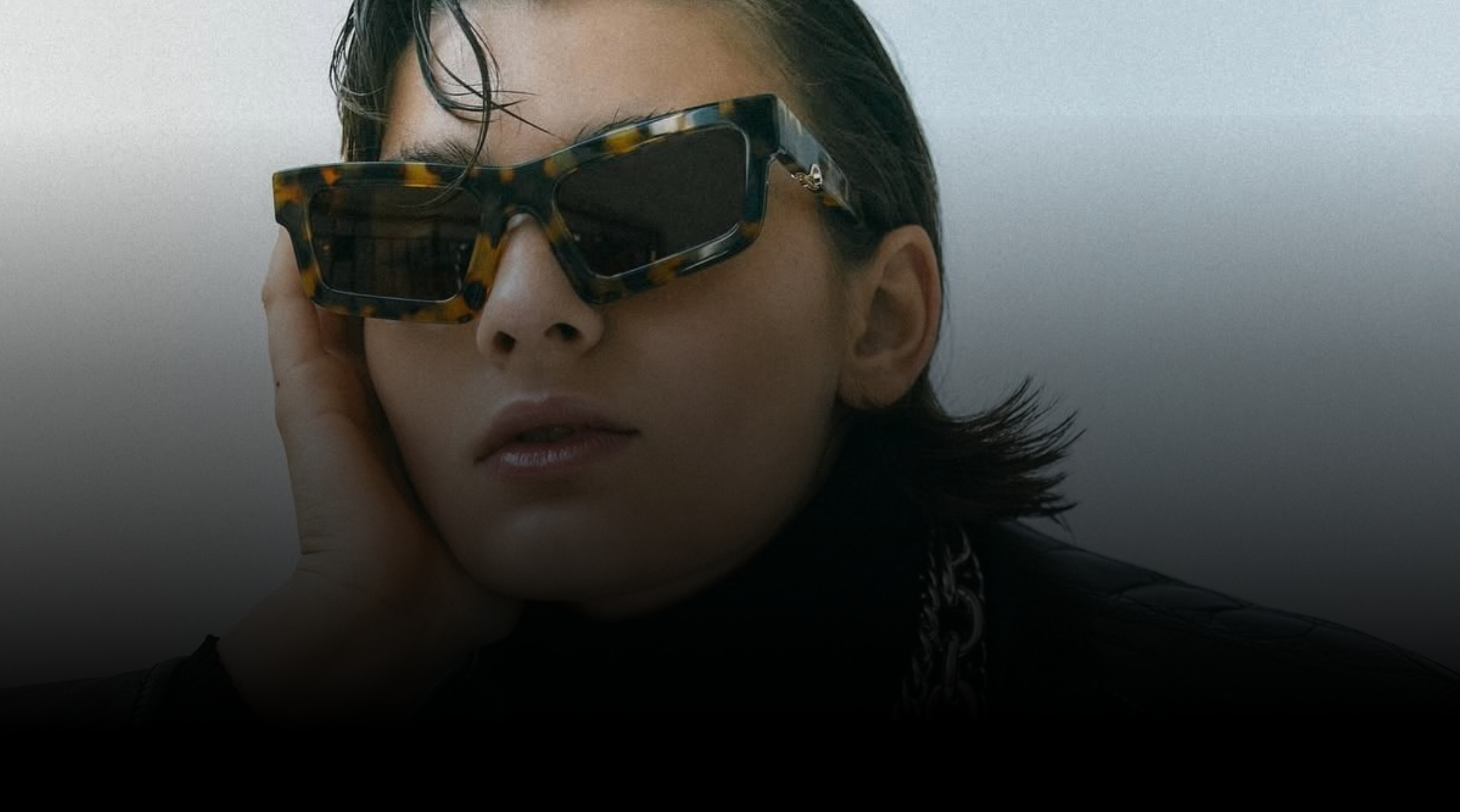 Person wearing tortoiseshell sunglasses with a neutral background