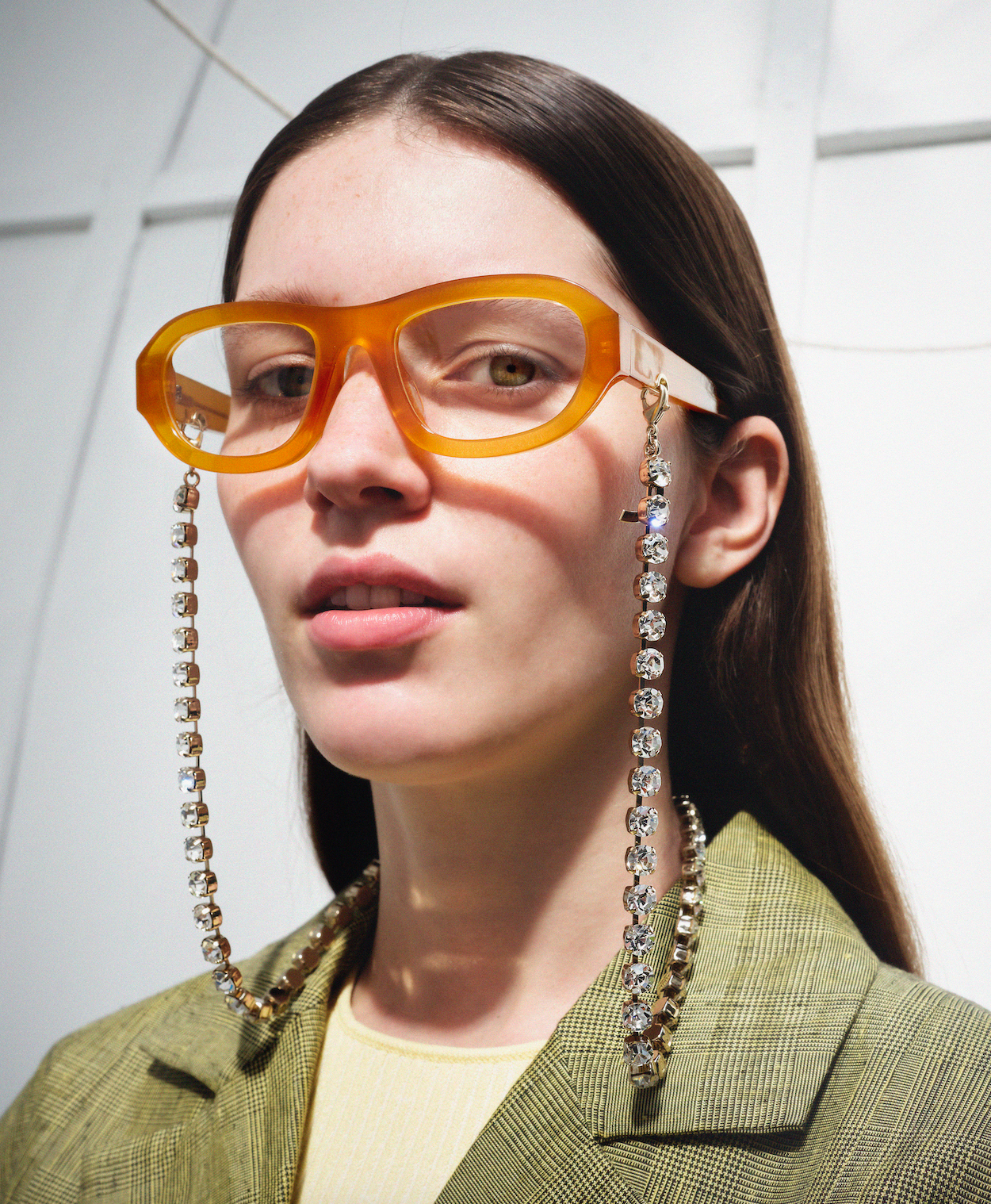 Person wearing large orange glasses with decorative chains, against a light background