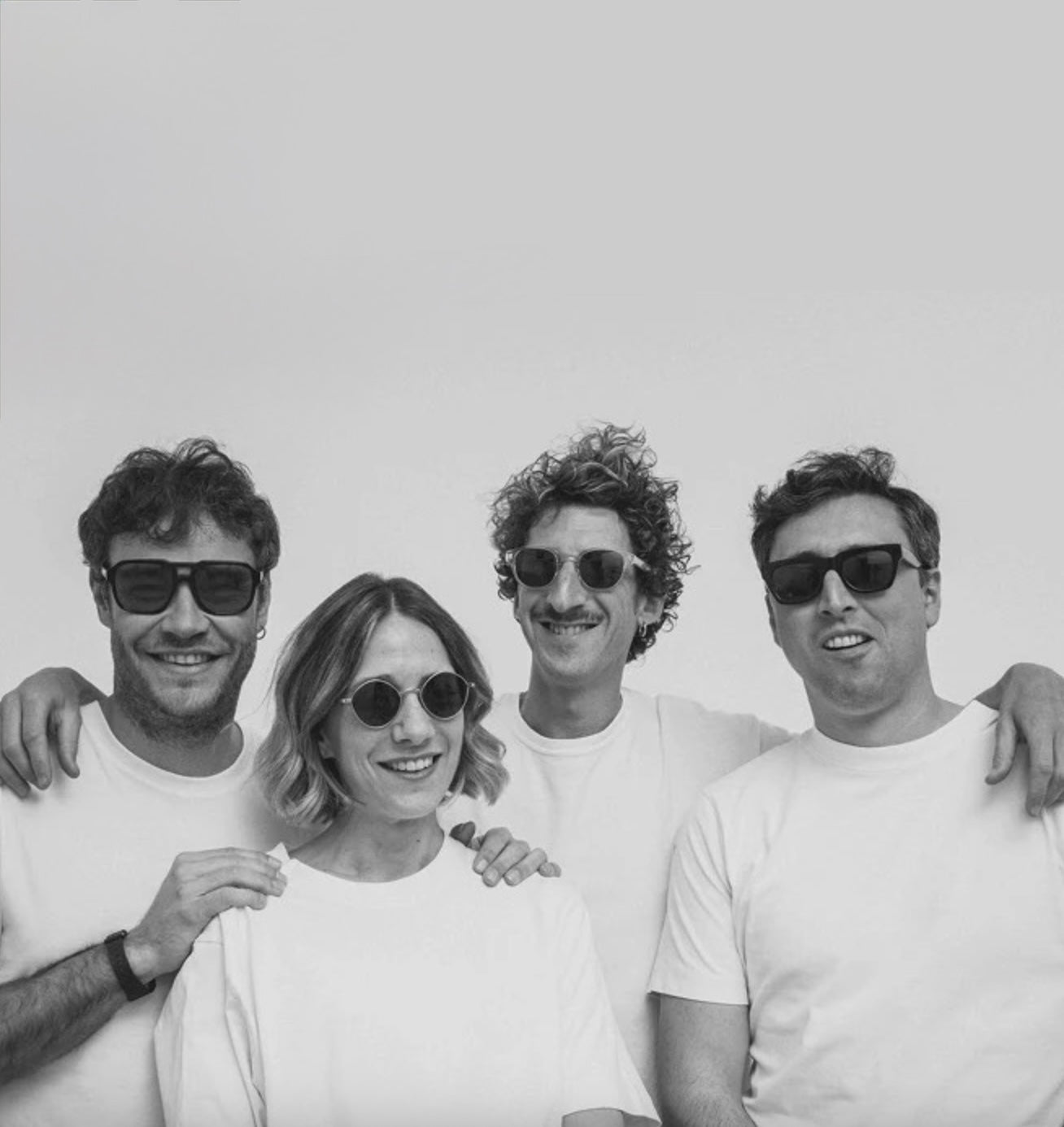 Four people wearing white t-shirts and sunglasses posing together against a plain light gray background.