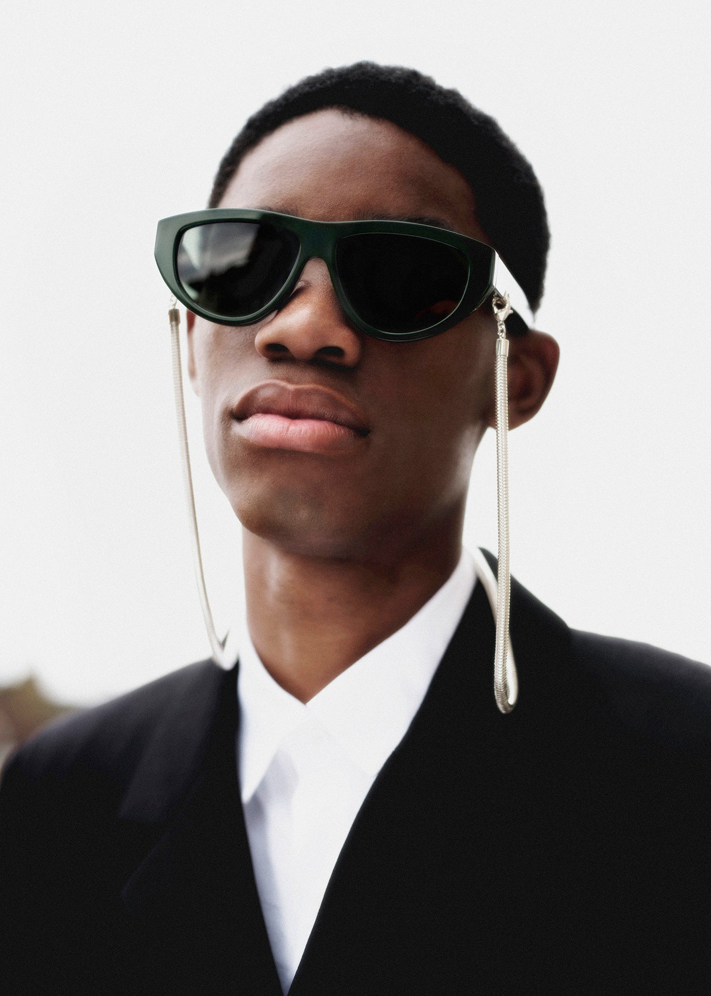 Person wearing dark sunglasses with long dangling earrings against a neutral background
