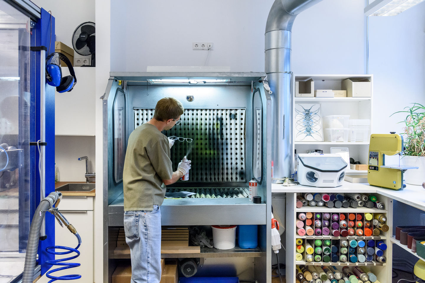 Person working in a laboratory or workshop setting with various equipment and supplies.